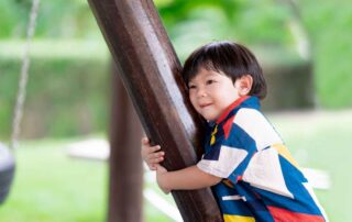 Child hugging wooden beam outdoors, displaying sensory-seeking behavior in a natural setting