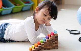 Young girl lying on the floor with learning materials, appearing disengaged—used to illustrate challenges supported by occupational therapy in Phnom Penh